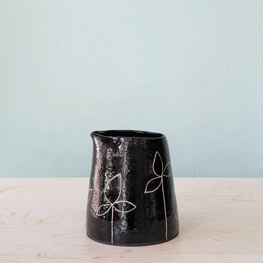 Black ceramic vase with white leaf patterns on a light wooden surface and light blue background