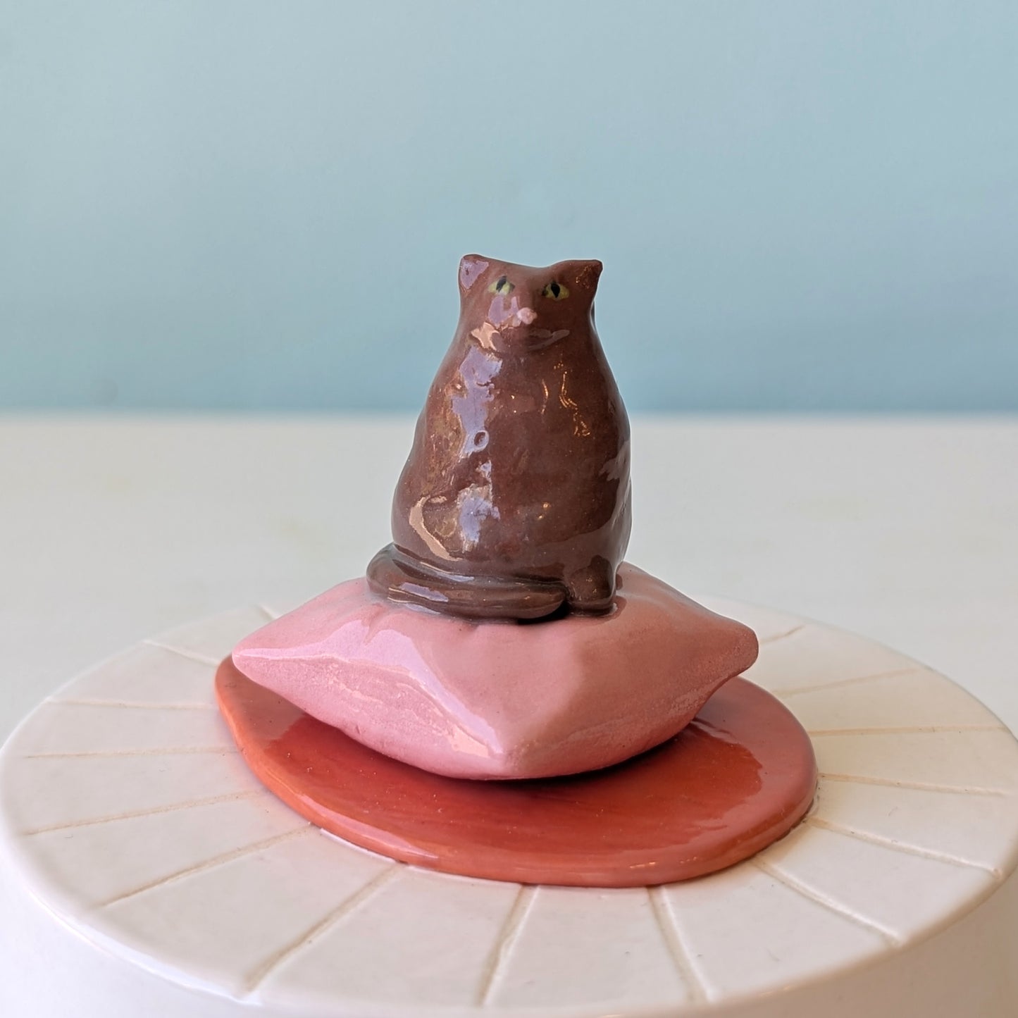 Ceramic cat figurine on a pink cushion with a blue background