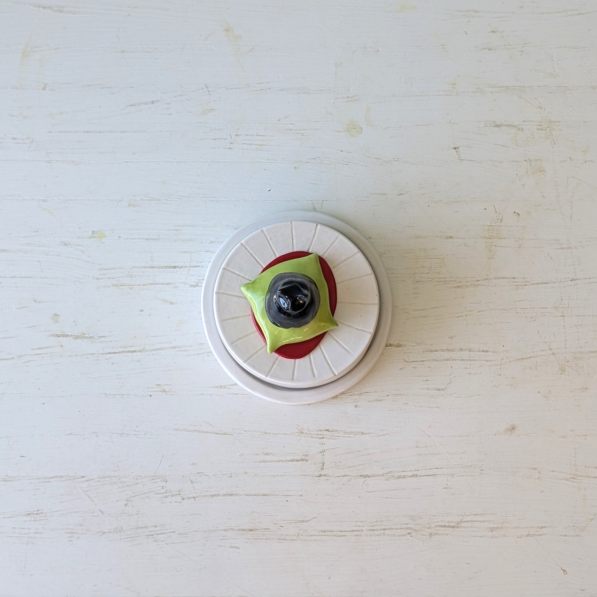 Round butter dish with white base, green top, and black center on a light wooden surface