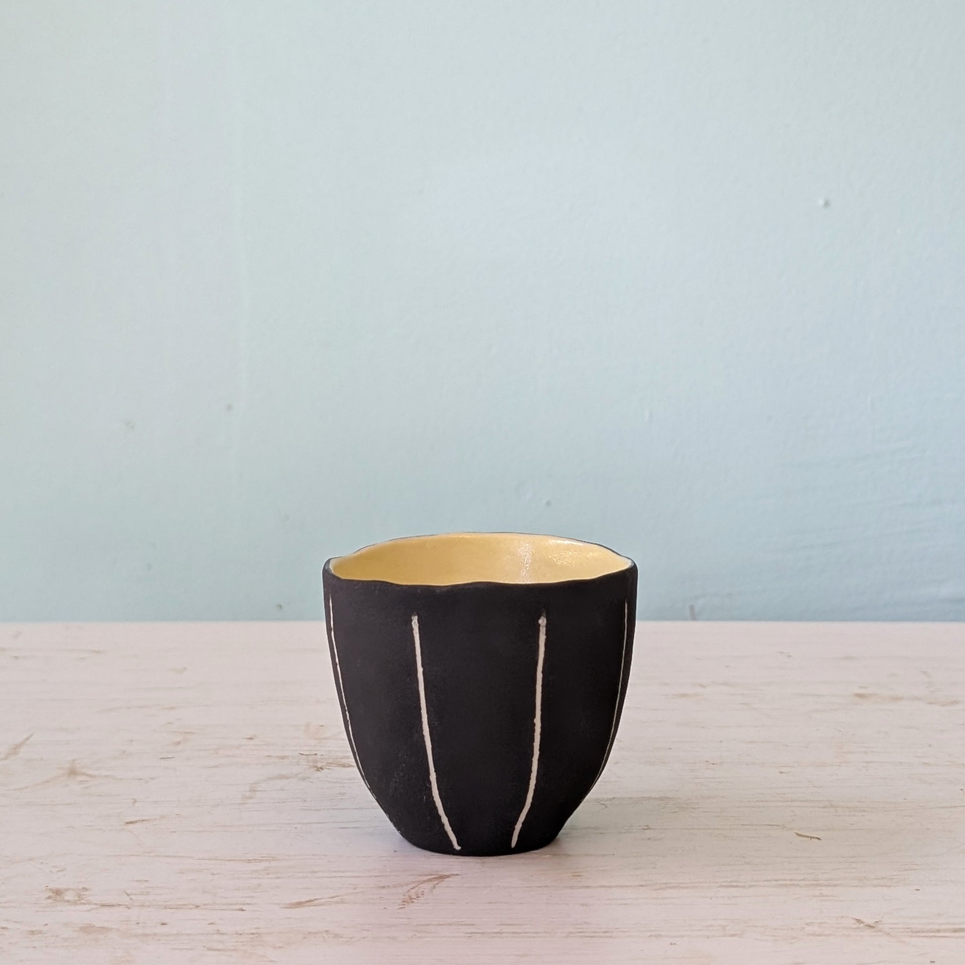 Black ceramic cup with yellow interior on a light wooden surface and blue background