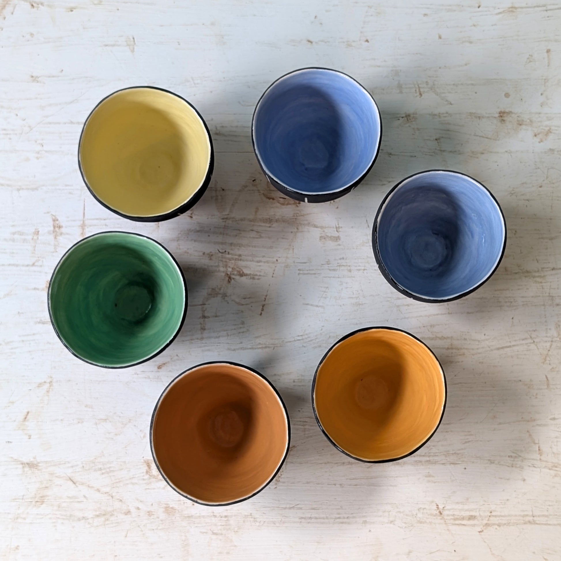 Six ceramic cups in different colors on a light wooden surface