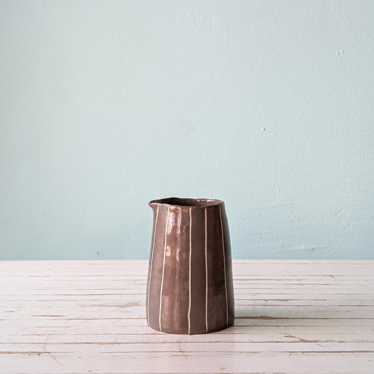 Front view of a brown ceramic pourer on a white wooden surface against a blue background.