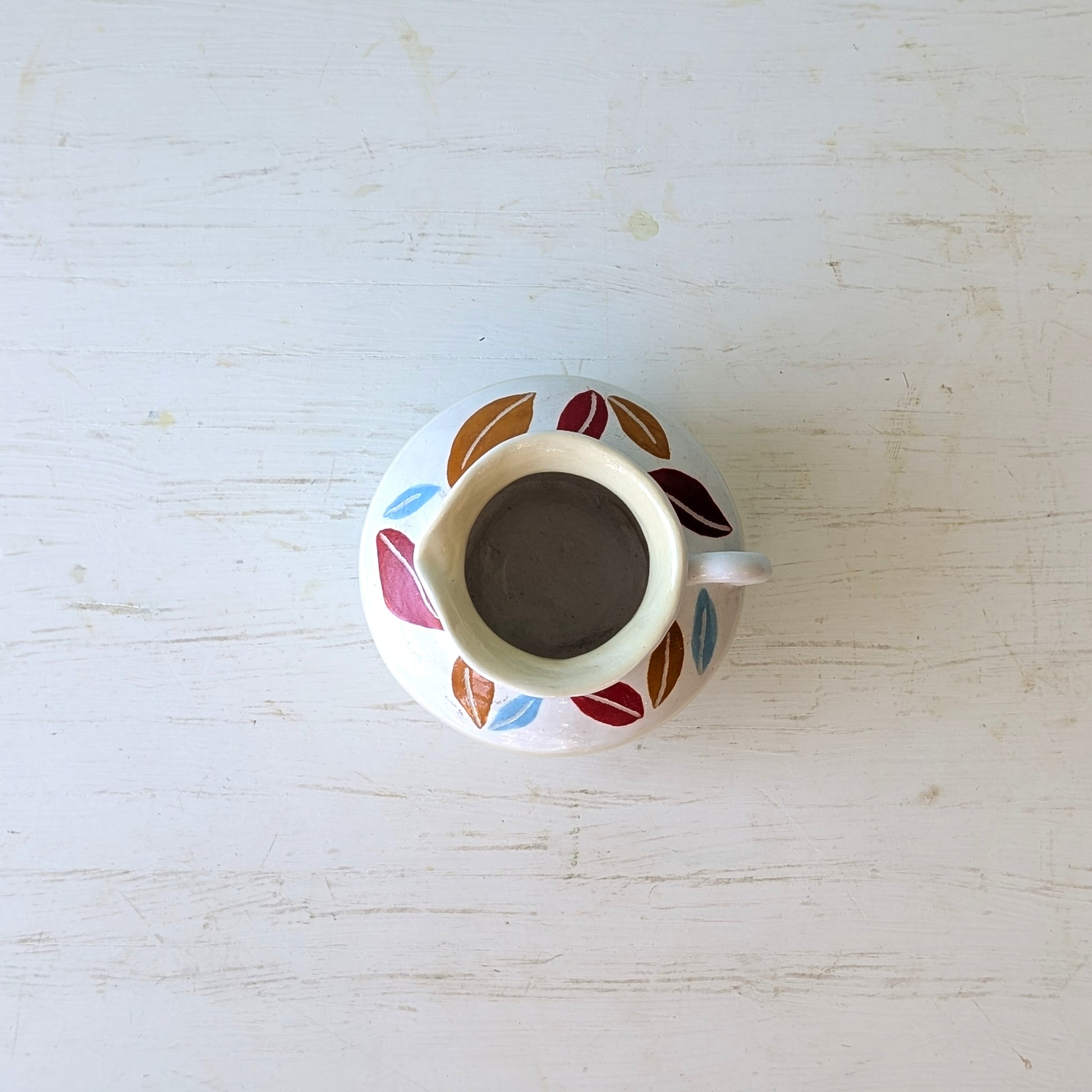 Small ceramic pitcher with colorful leaf patterns on a white surface