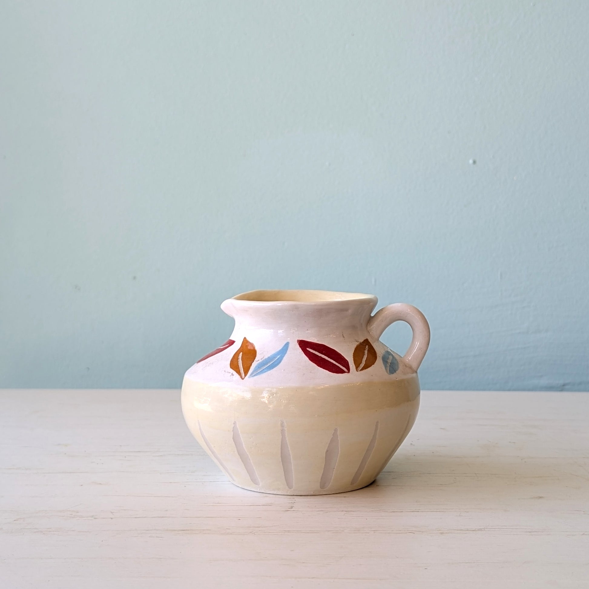 Ceramic jug with colorful leaf patterns on a light blue background