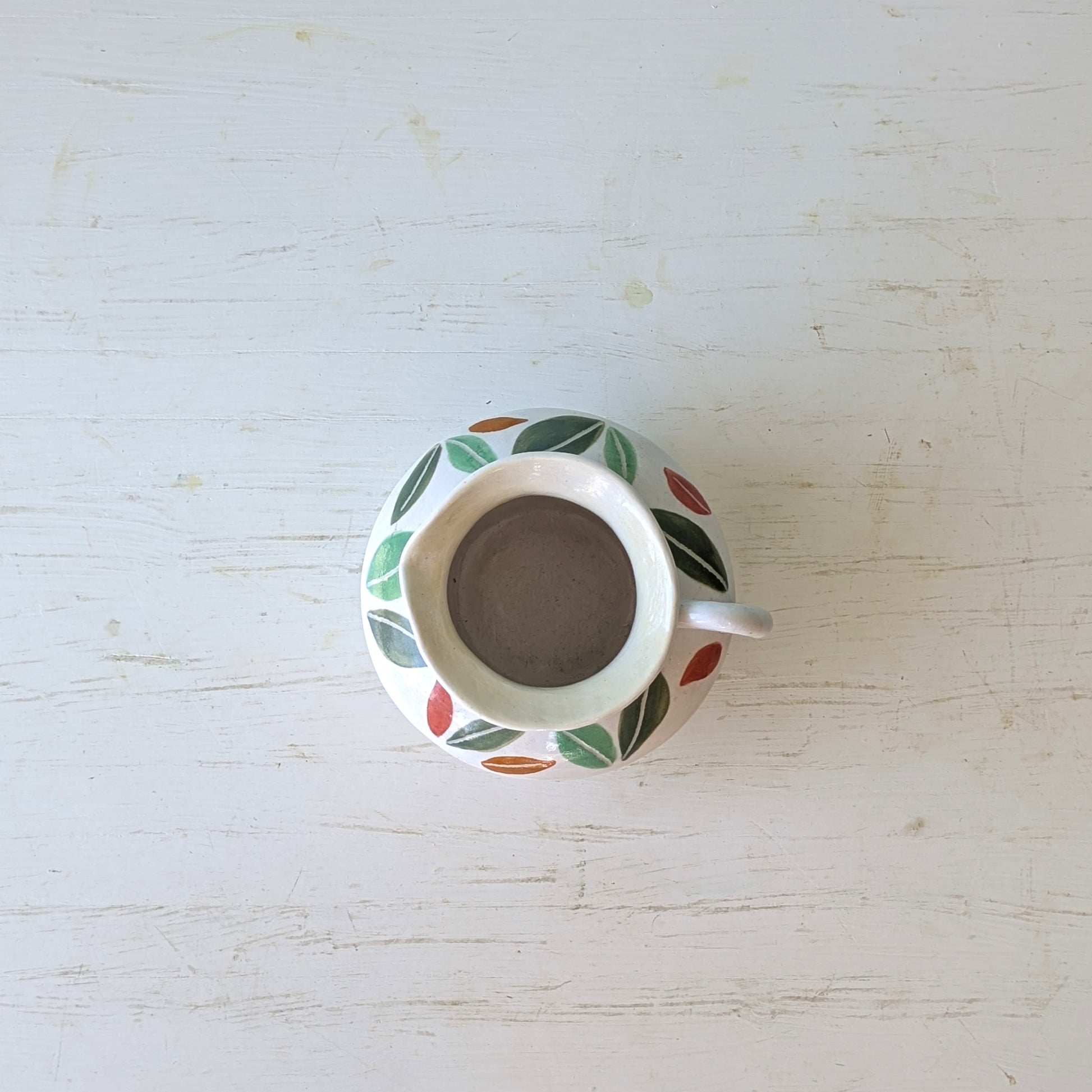 White ceramic jug with leaf design on a light wooden surface