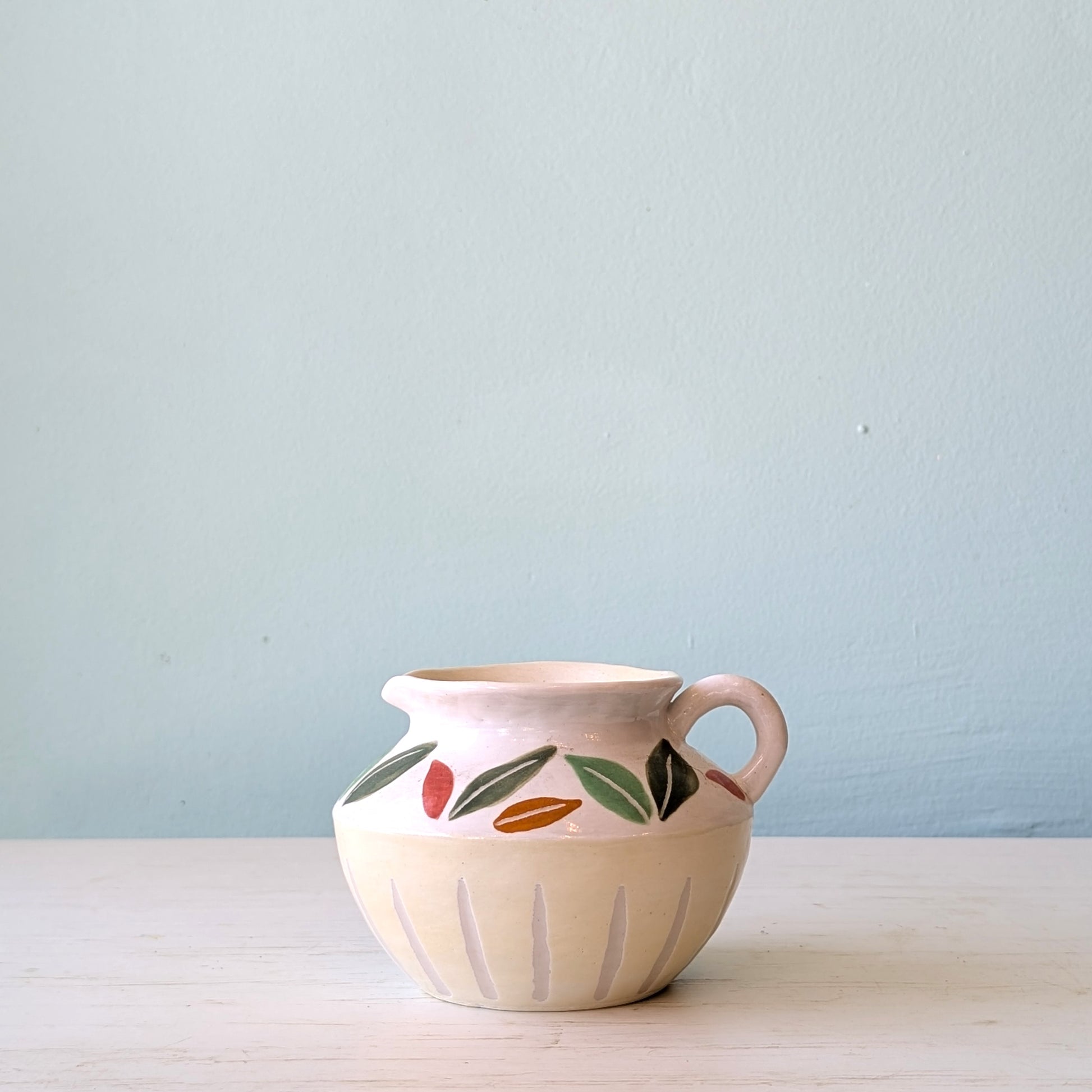 Ceramic jug with leaf pattern on a white table against a blue wall