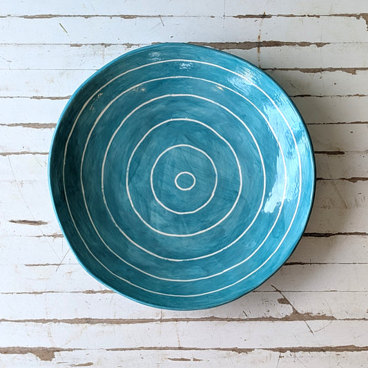 Top view of a blue ceramic plate with carved concentric circles on a white wooden surface.