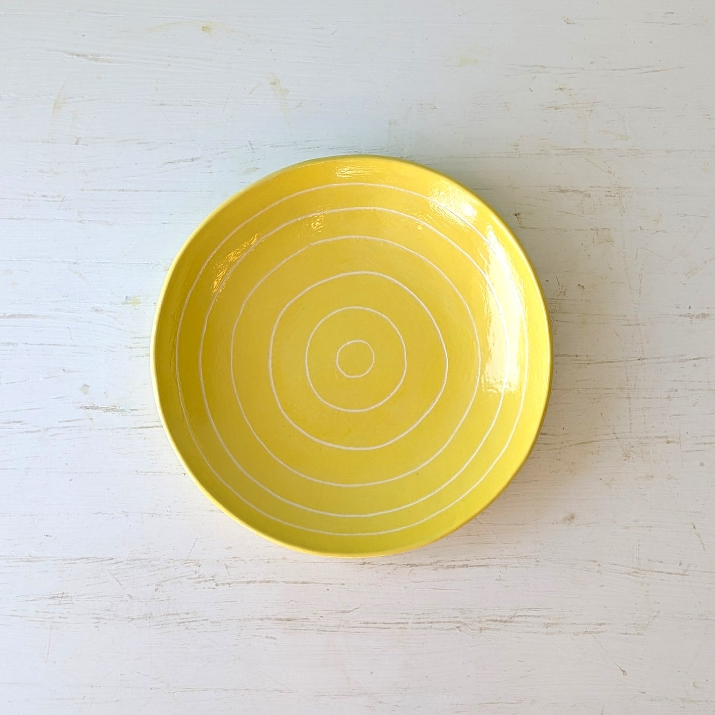 Yellow ceramic plate with carved concentric circles on a white table
