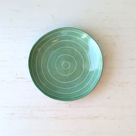 Green ceramic plate with carved concentric circles on a white table