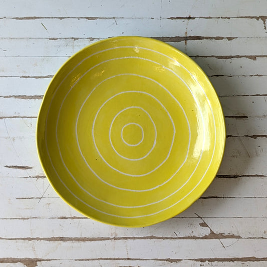 Top view of a yellow ceramic plate with carved concentric circles on a white wooden surface.