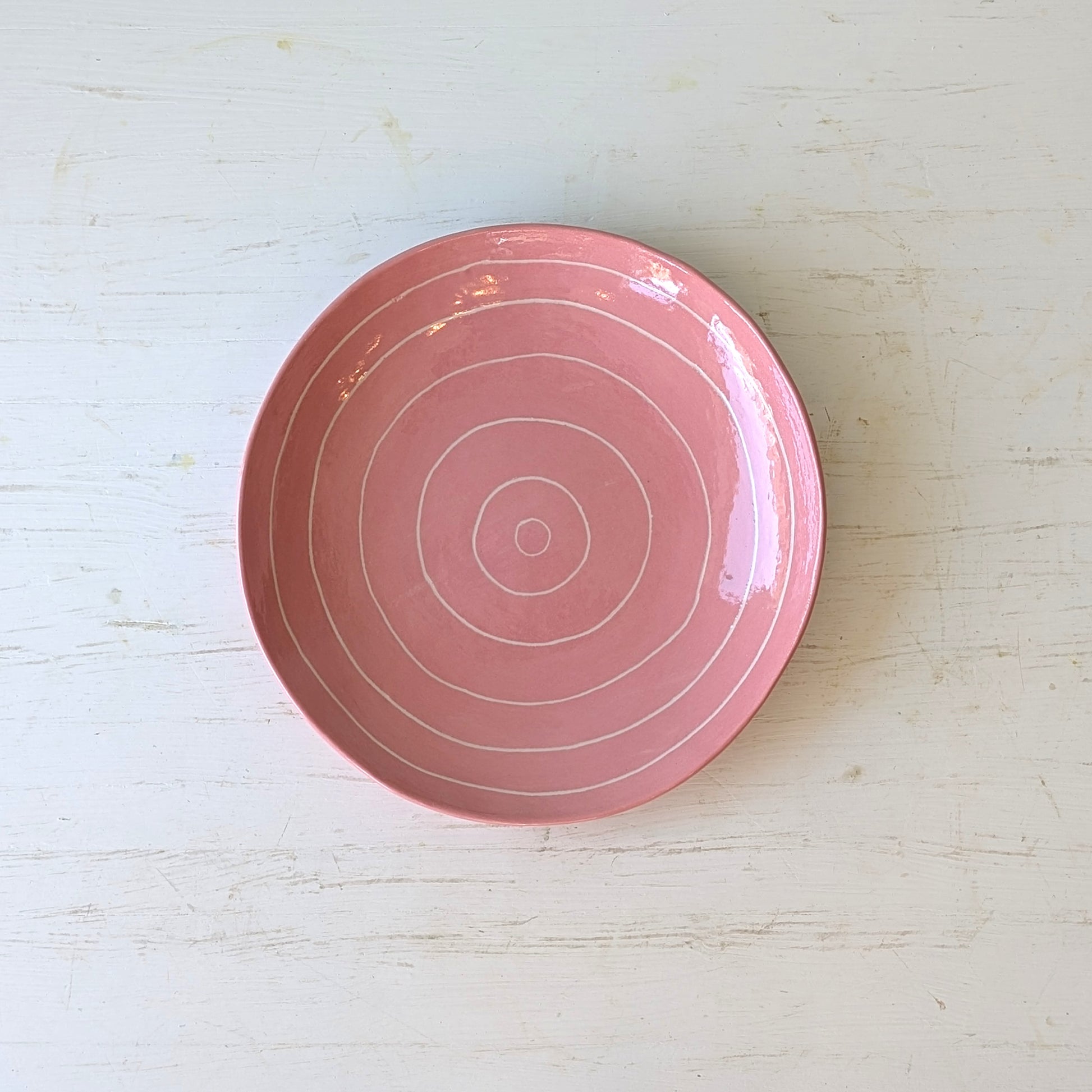 Pink ceramic plate with carved concentric circles on white table