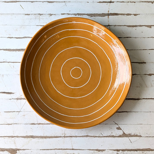 Top view of an orange ceramic plate with carved concentric circles on a white wooden surface.
