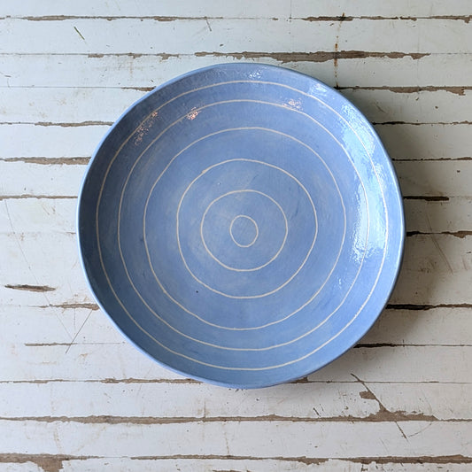Top view of a blue ceramic plate with carved concentric circles on a white wooden surface.