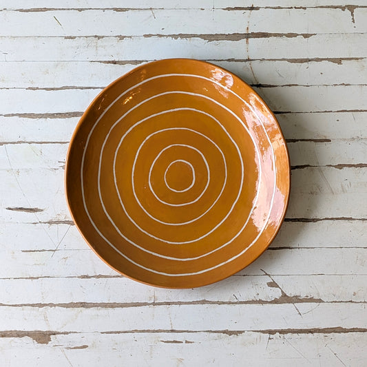Top view of an orange ceramic plate with carved concentric circles on a white wooden surface.