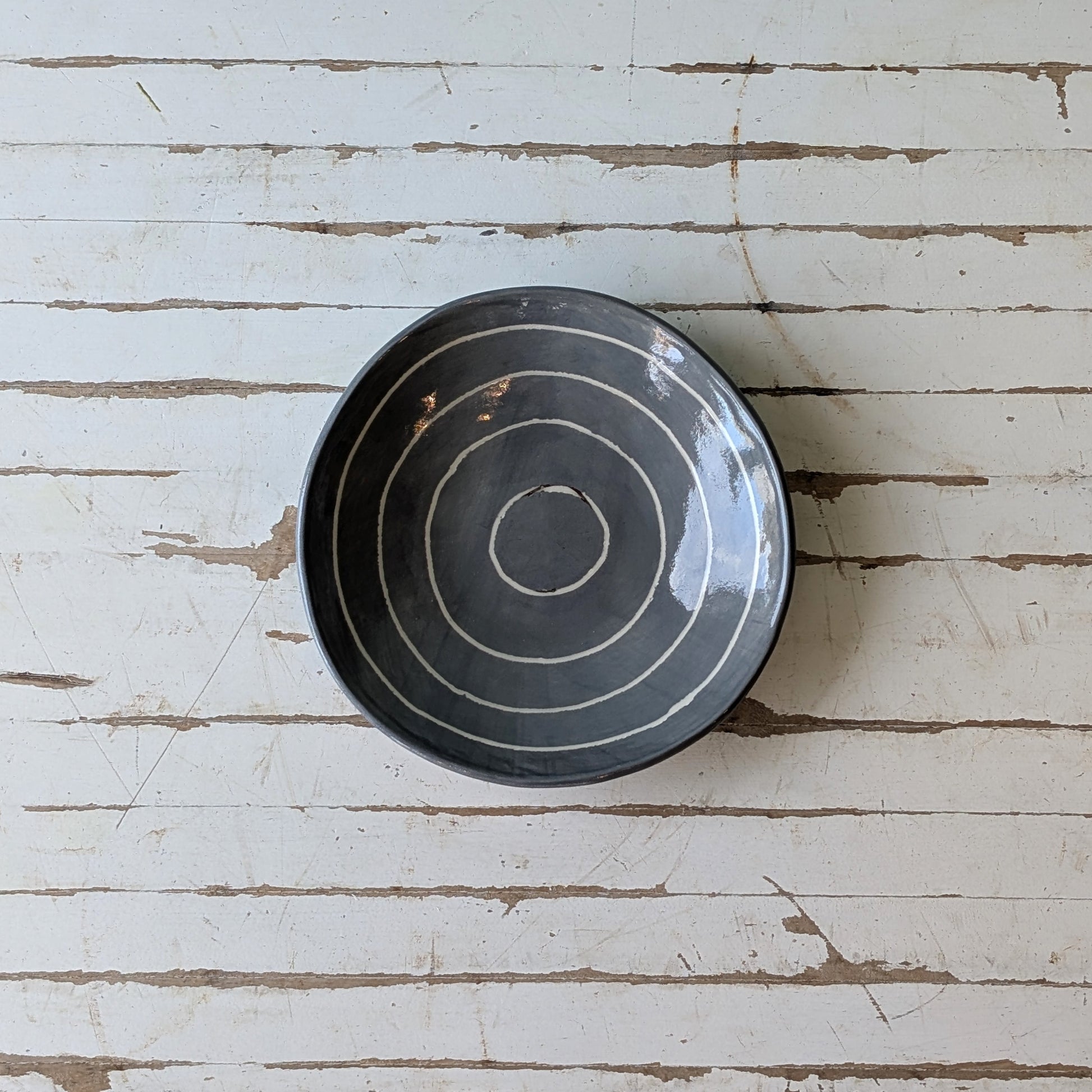 Top view of a grey ceramic bowl with carved concentric circles on a white wooden table.