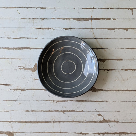 Top view of a grey ceramic bowl with carved concentric circles on a white wooden table.