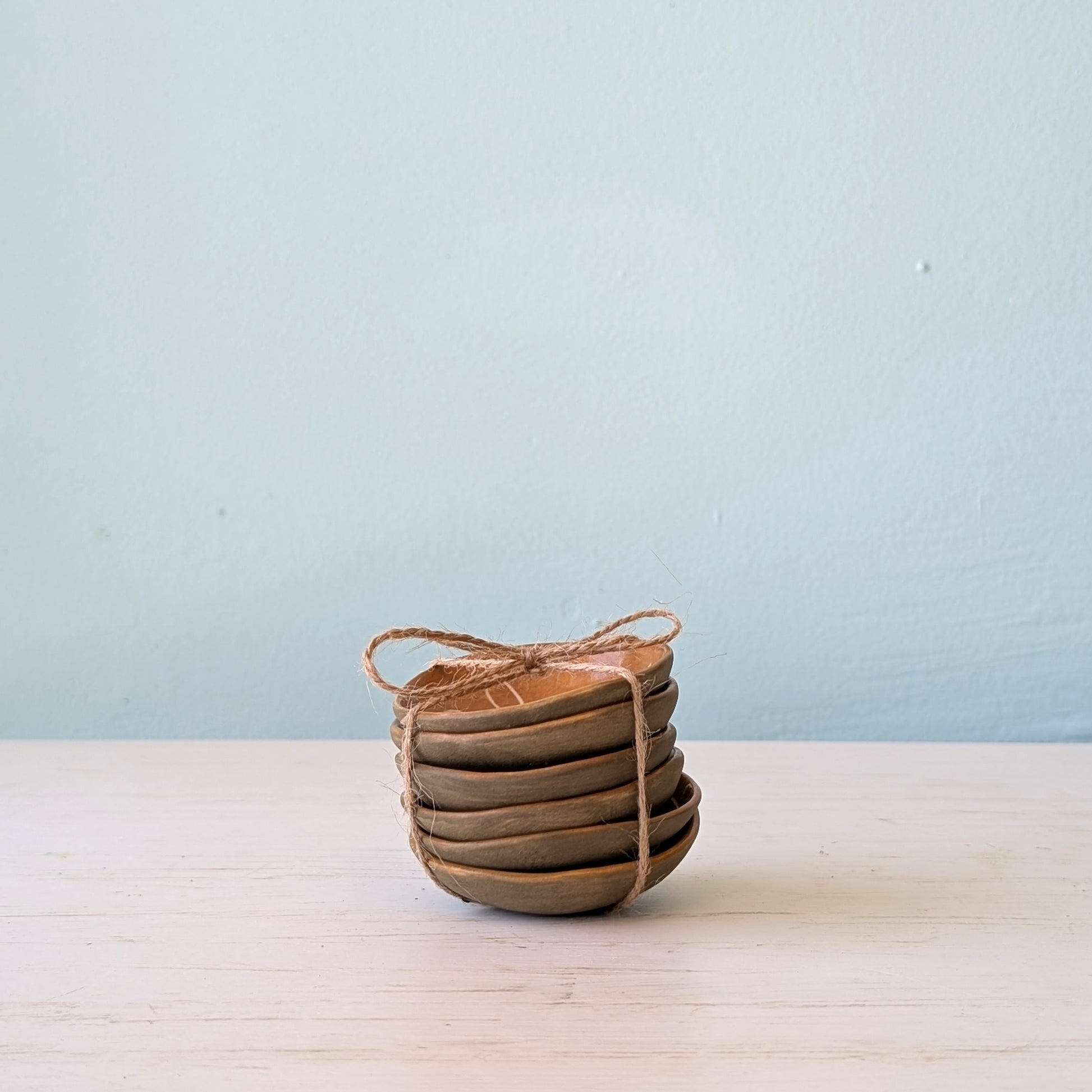 Stack of small brown ceramic bowls tied with twine on a light wooden surface with a light blue background