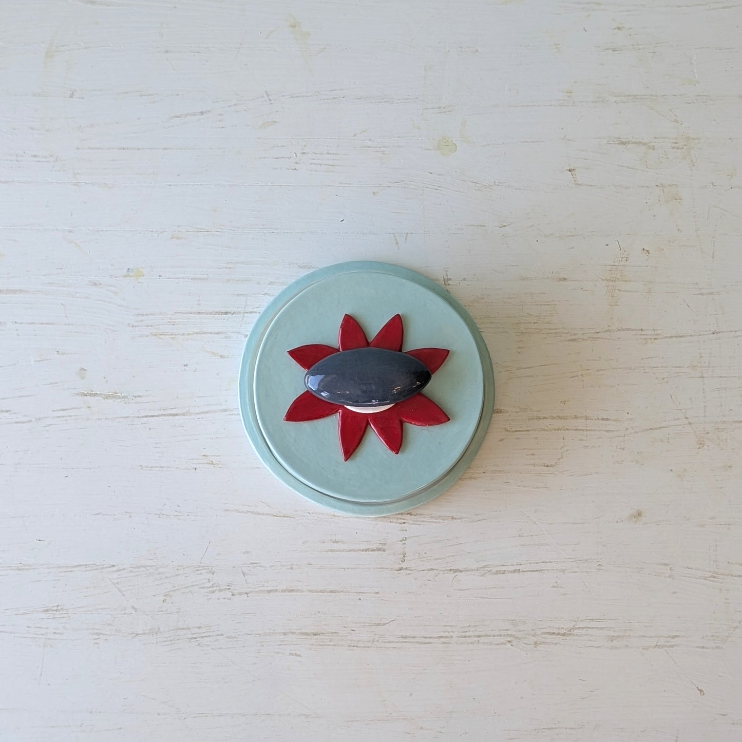 Blue ceramic butter dish with a red flower and grey pebble design on a light blue background
