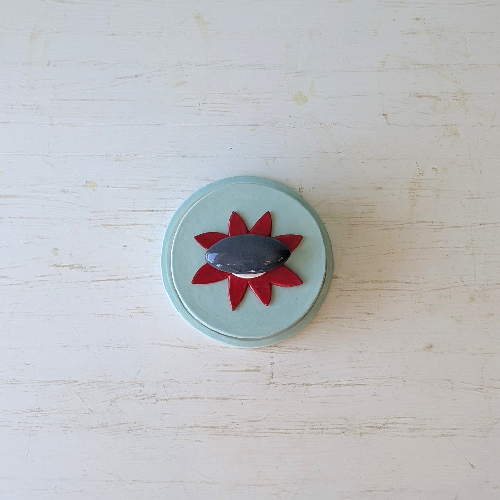 Blue ceramic butter dish with a red flower and grey pebble design on a light blue background