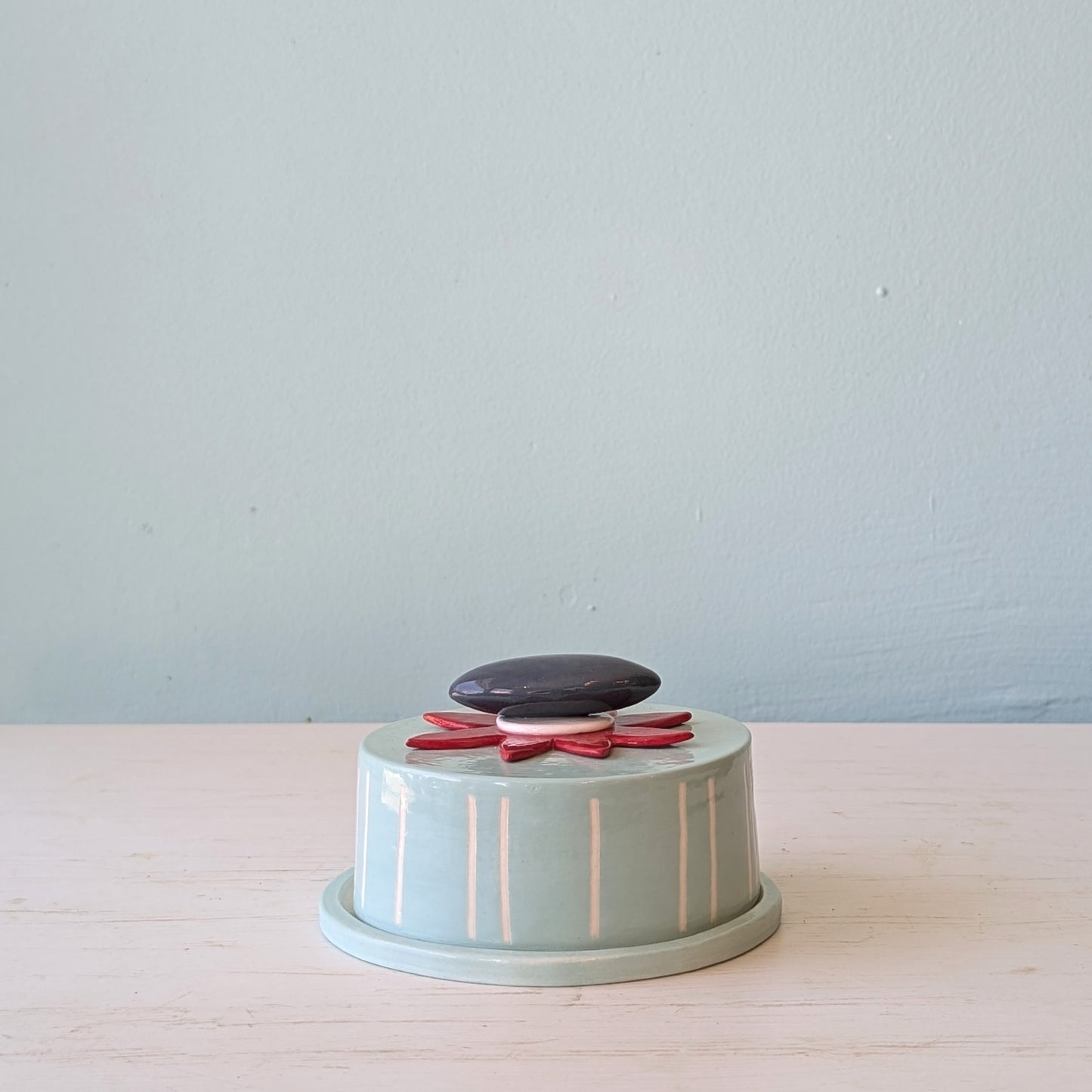 Light blue ceramic butter dish with decorative stones on a light wooden surface and light blue background
