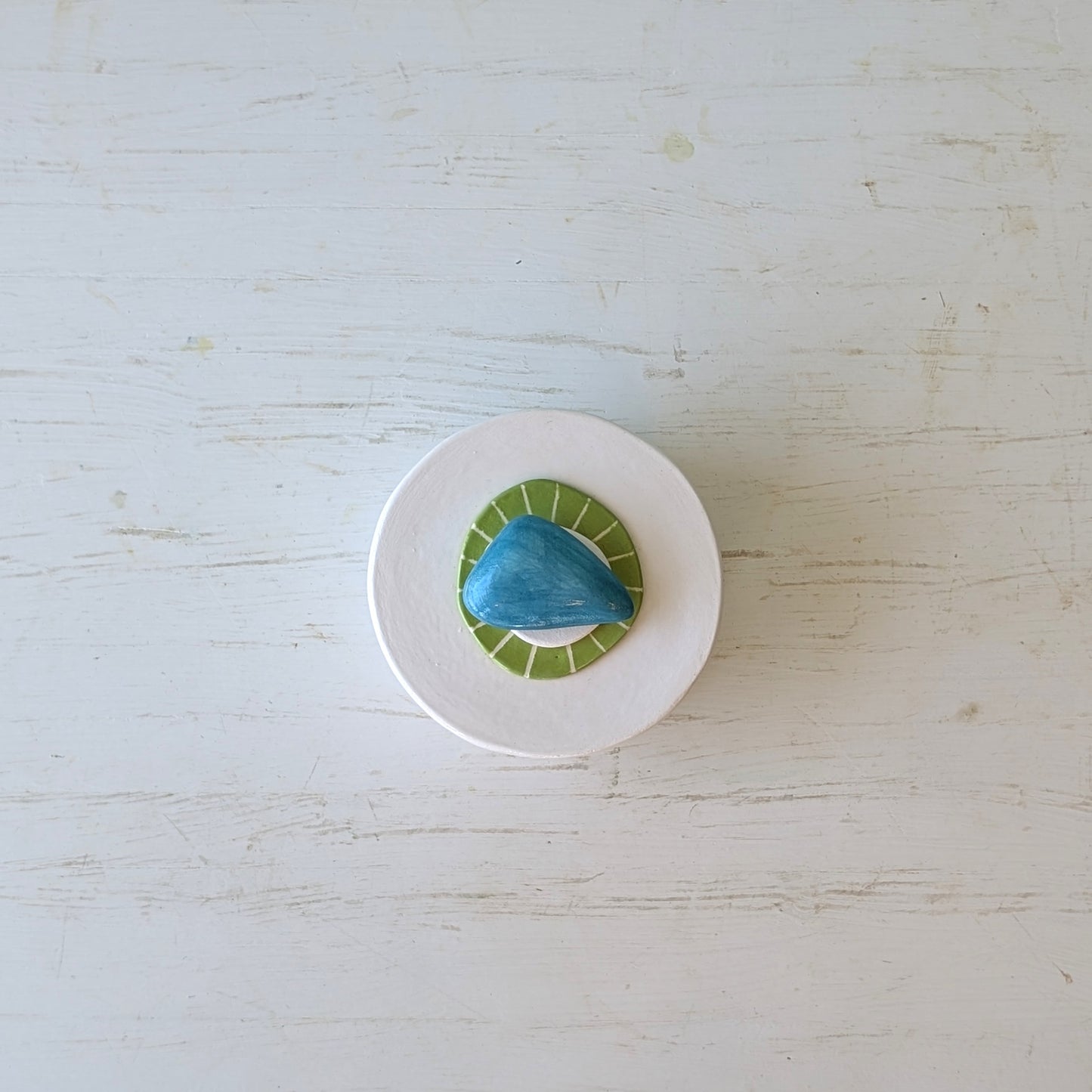 Round ceramic butter dish with blue and green pebble design on a light wooden surface