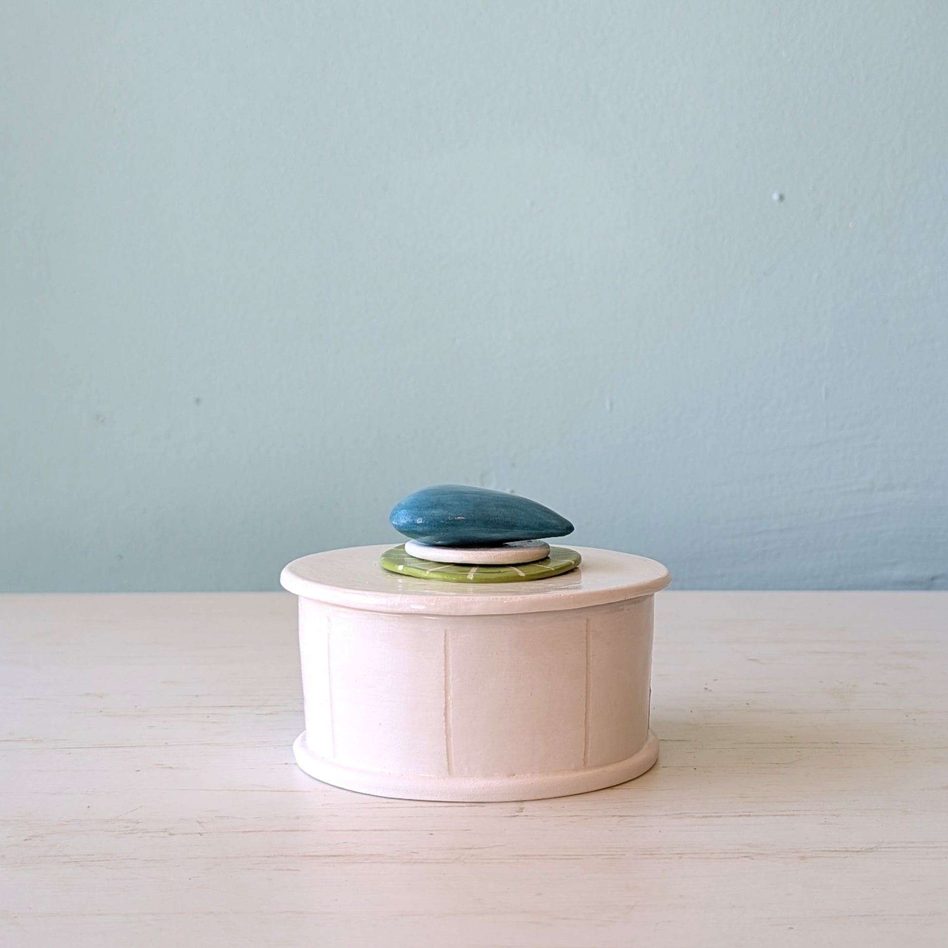 White ceramic butter dish with a blue pebble design on lid on a light blue background