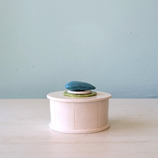 White ceramic butter dish with a blue pebble design on lid on a light blue background