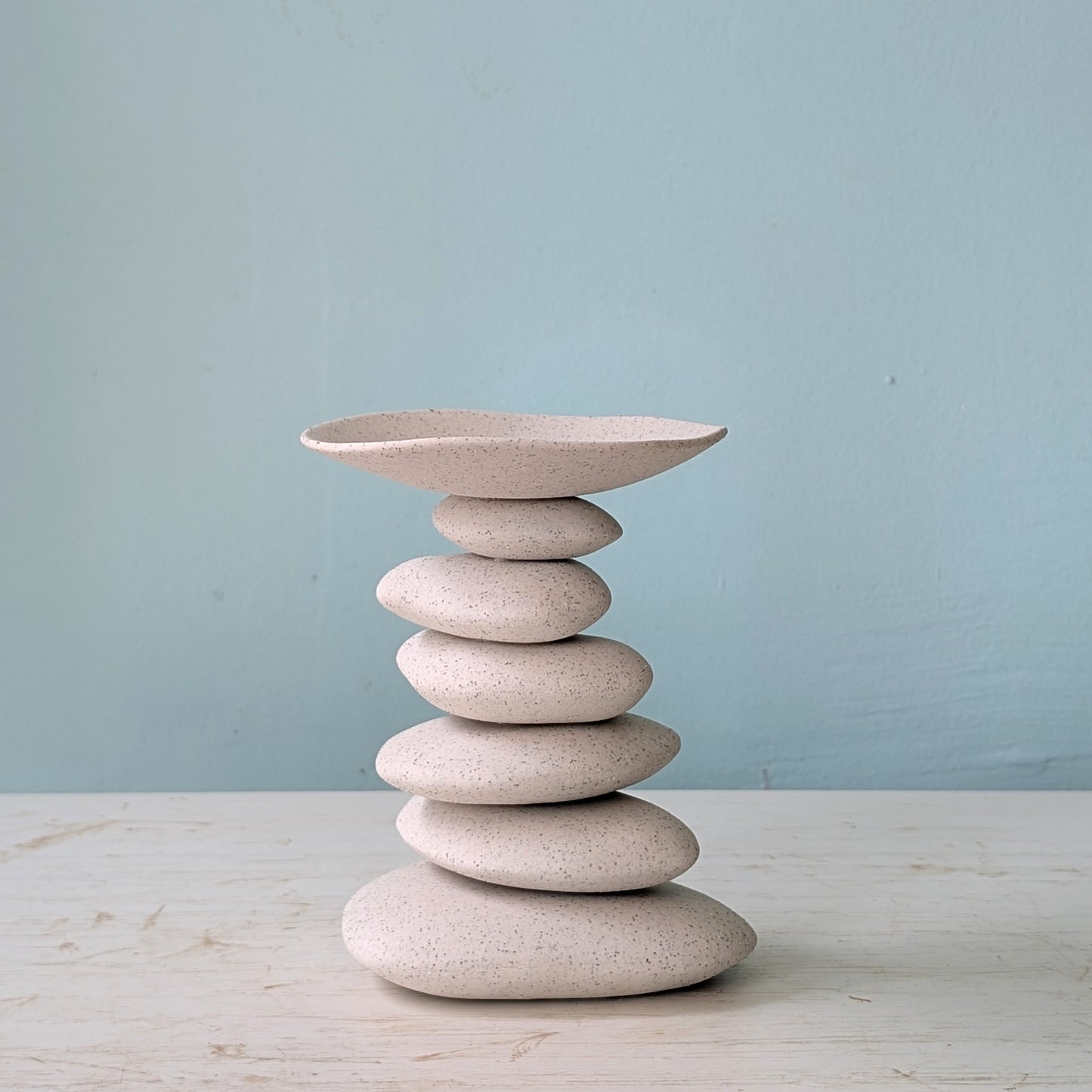 Ceramic candlestick resembling a stack of stones with a bowl on top against a light blue background