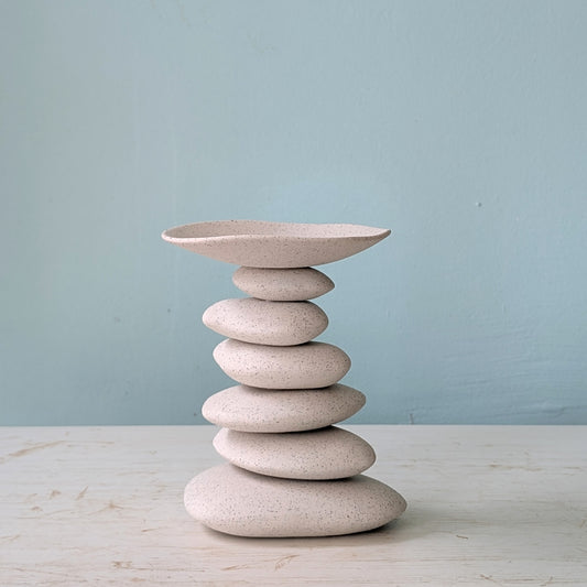 Ceramic candlestick resembling a stack of stones with a bowl on top against a light blue background