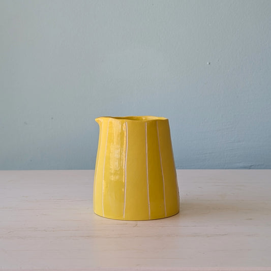 Yellow ceramic jug on a white table against a blue wall