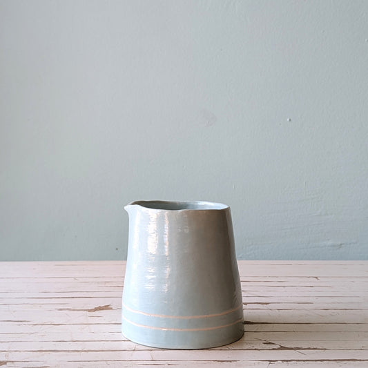 Front view of a light blue pourer on a white wooden surface against a blue background.
