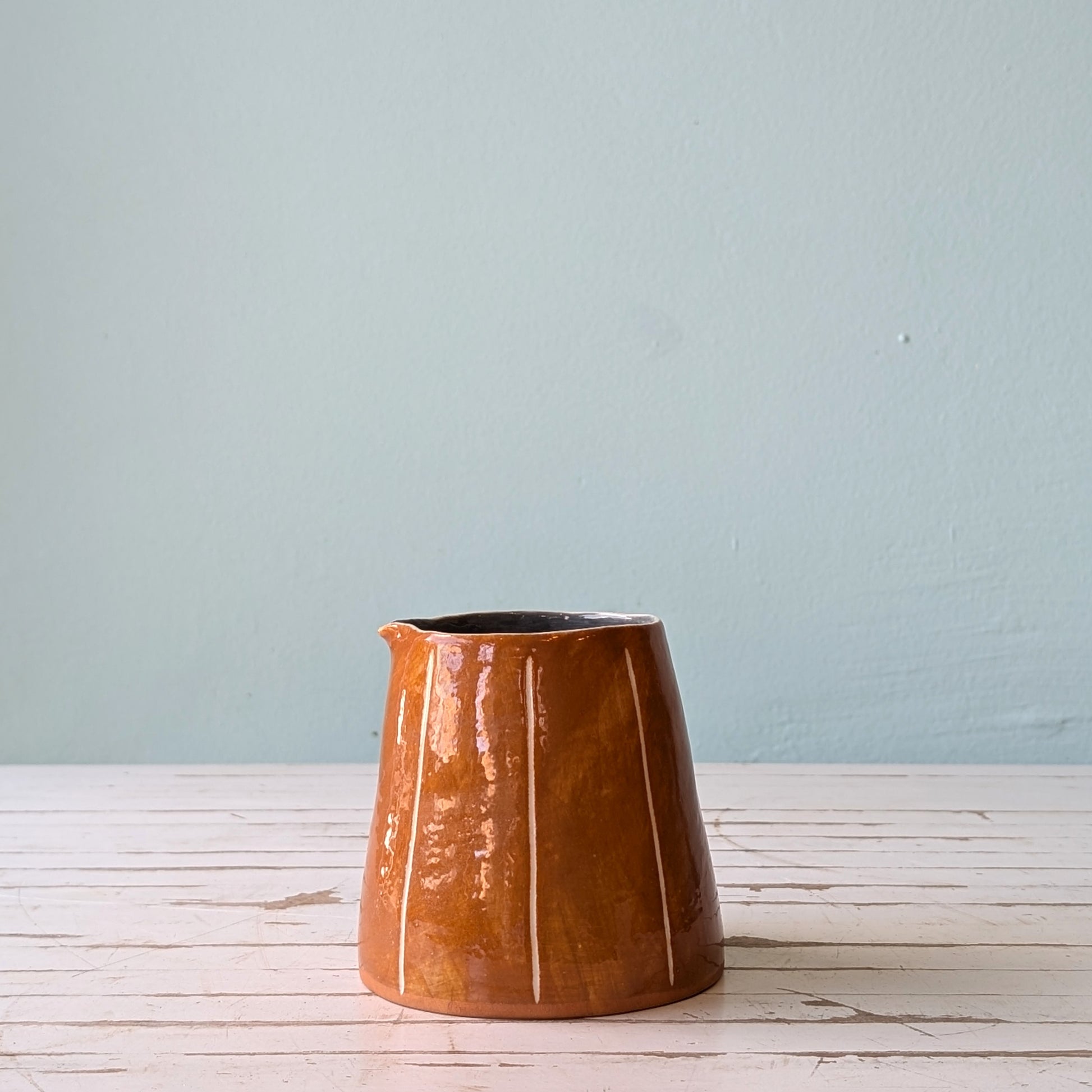 Front view of a brown ceramic pourer on a white wooden surface against a blue background.