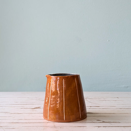 Front view of a brown ceramic pourer on a white wooden surface against a blue background.