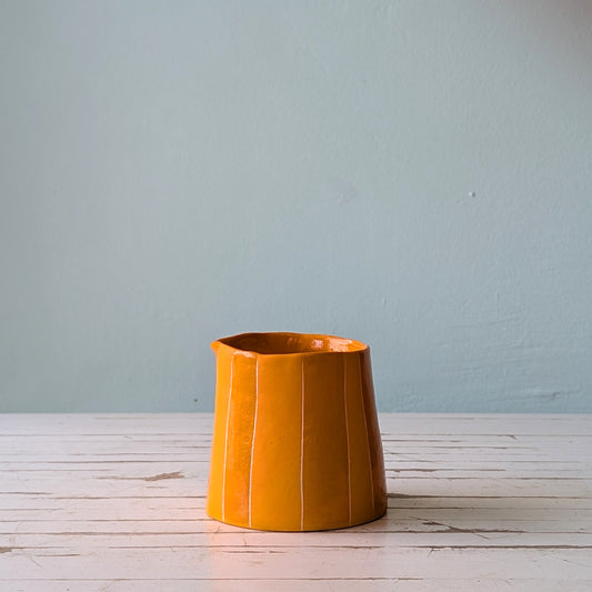 Front view of an orange ceramic pourer on a white wooden surface with a blue background.