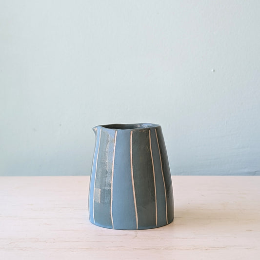 Small teal jug on white table against a blue wall