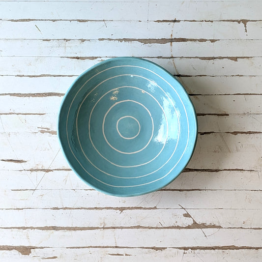 Top view of a blue ceramic bowl with carved concentric circles on a white wooden surface.