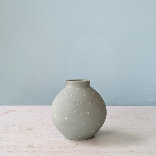 Seafoam ceramic vase with white polka dots on a white table against a blue wall.