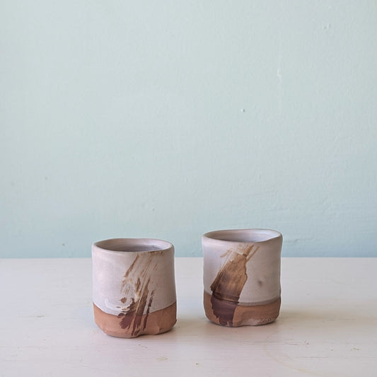 Two ceramic cups with natural brown and white design on a light blue background