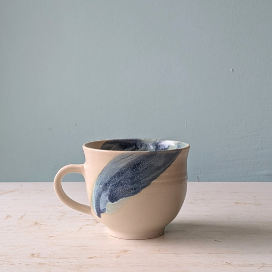 Ceramic mug with blue and beige design on a light wooden surface and gray background