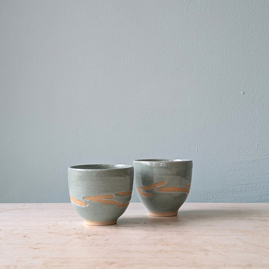 Two small ceramic cups without handles in a light blue/green glaze