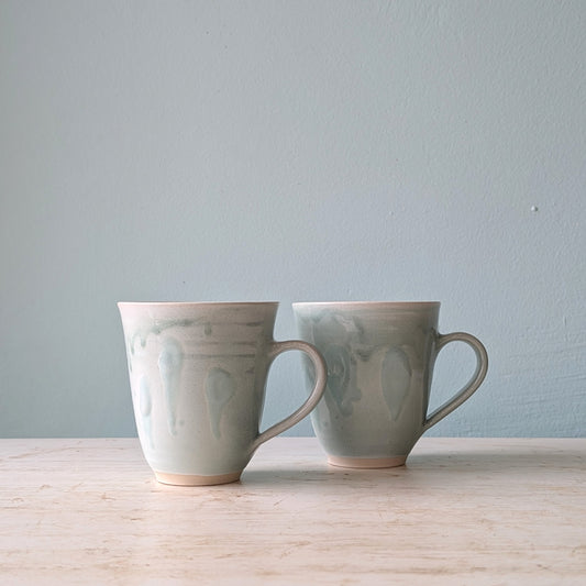Two ceramic mugs with textured azure blue surface, on a white table against a light blue wall.