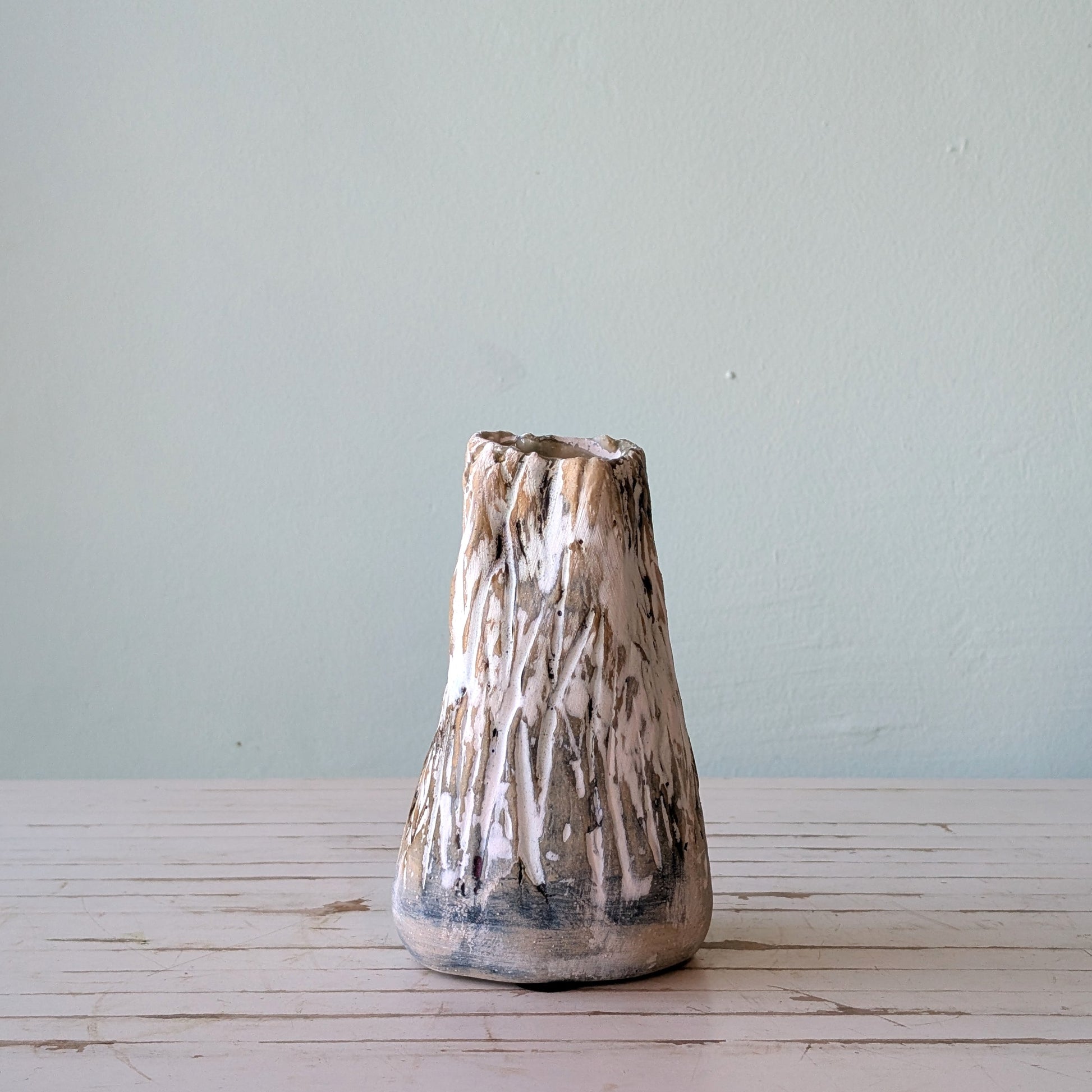 Front view of a beige stoneware vase with thick black and white glaze and vertical scoring, resembling the surface of tree bark.