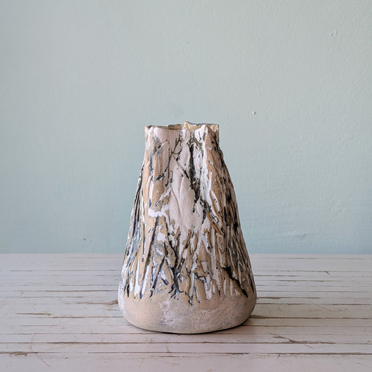 Front view of a beige stoneware vase with thick black and white glaze and vertical scoring, resembling the surface of tree bark.