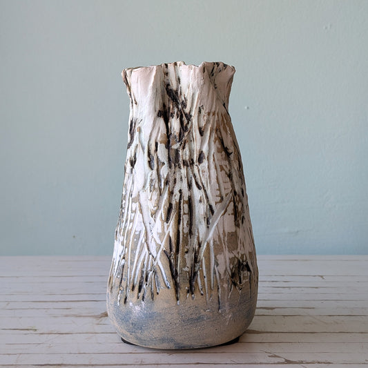 Front view of a beige stoneware vase with thick black and white glaze and vertical scoring, resembling the surface of tree bark.