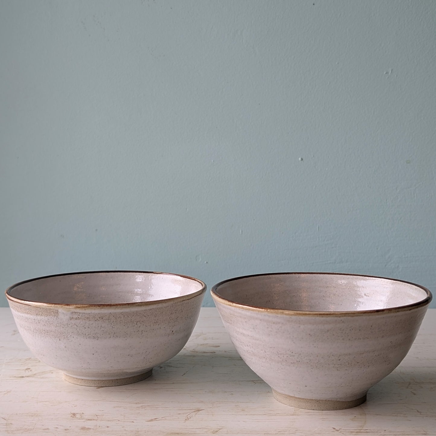 Two beige ceramic bowls on a white table against a blue wall