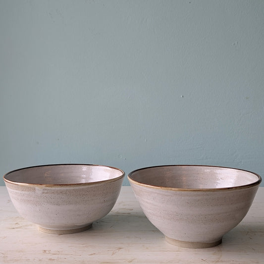 Two beige ceramic bowls on a white table against a blue wall