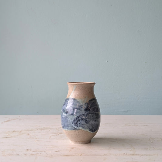 Ceramic vase with blue and green marbled pattern on a light wooden surface with a light gray background