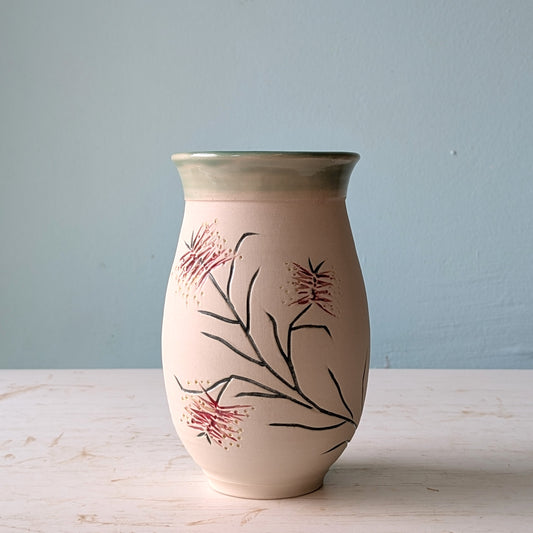 Ceramic vase with floral bottlebrush design on a light wooden surface and blue background