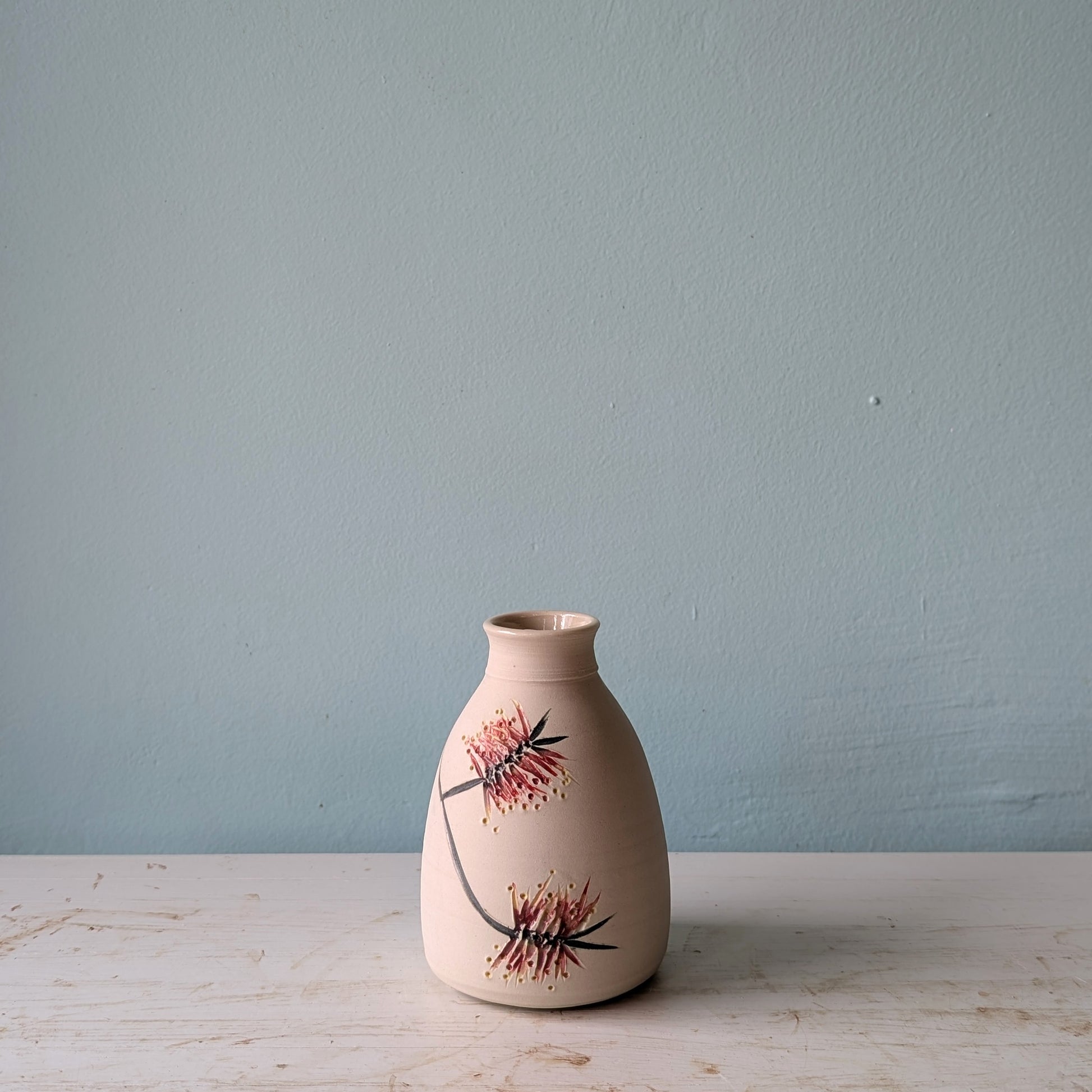 Ceramic vase with floral bottlebrush pattern on a white table against a blue wall.