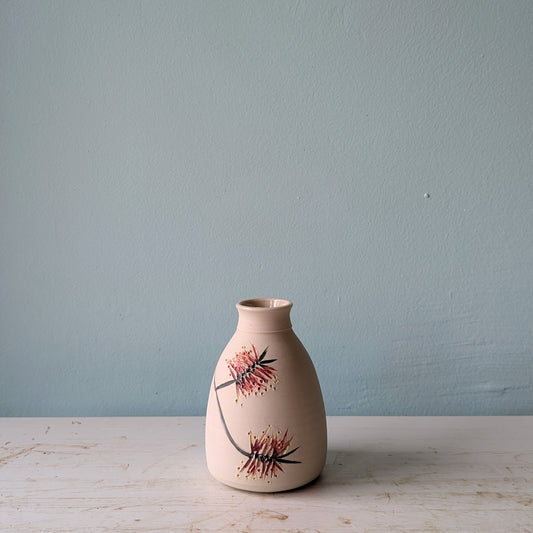 Ceramic vase with floral bottlebrush pattern on a white table against a blue wall.